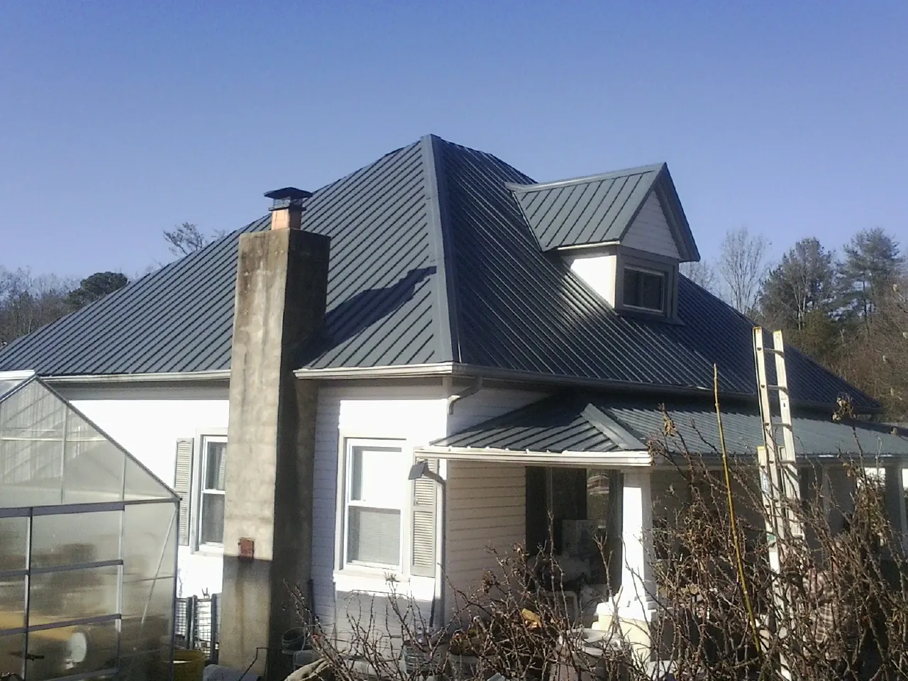 Dark blue standing seam metal roof on a white farmhouse with dormer — Slate & Tile Roof Repair by Roofing Brothers in Kittrell