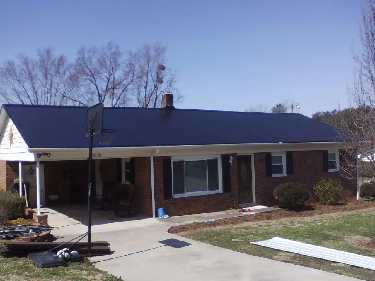 Finished dark blue metal roof on a brick ranch with a carport in Kittrell