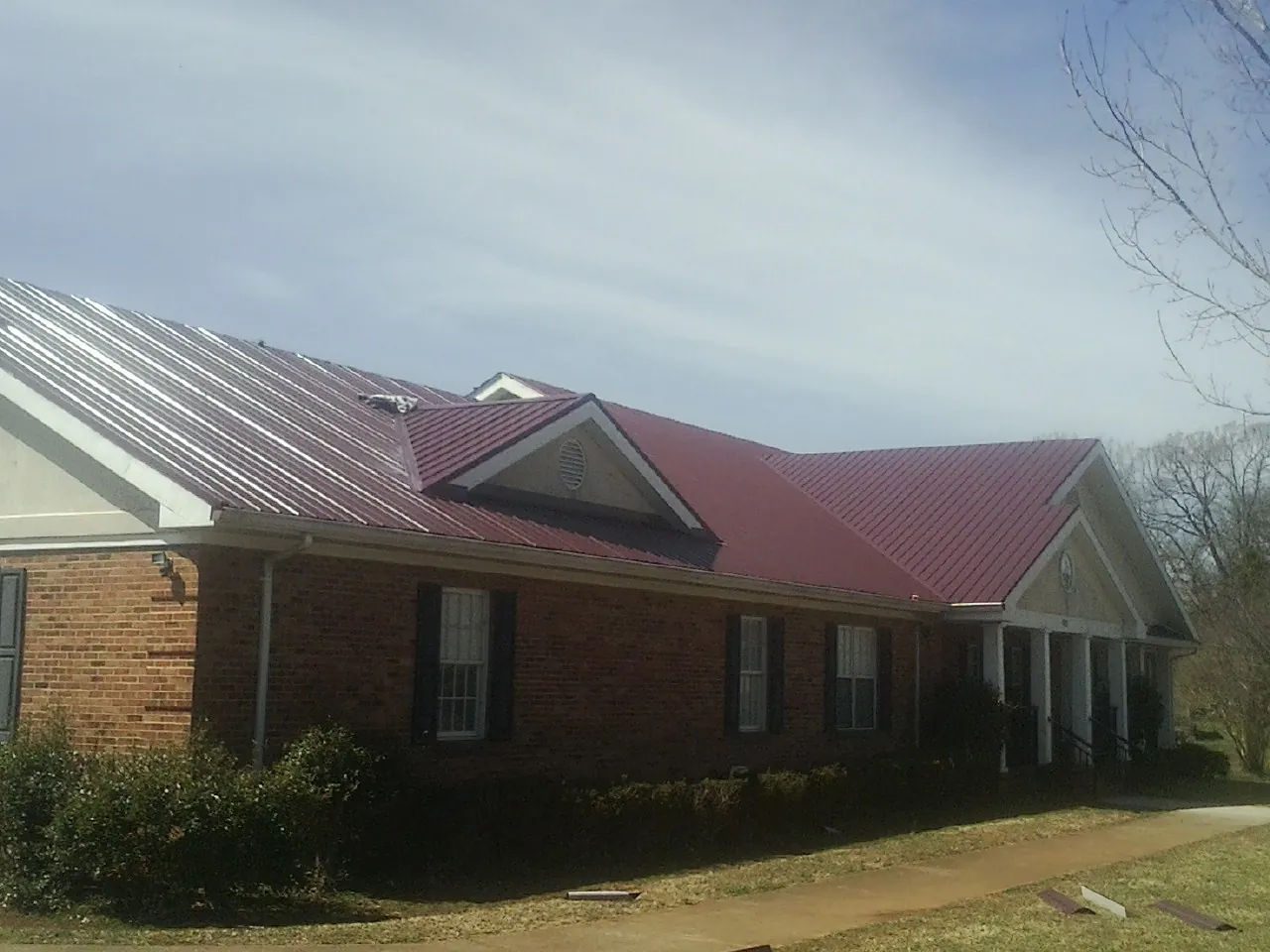 Red metal roof with gabled entries on a long brick building, from a Hail Damage Roof Repair job in Kittrell