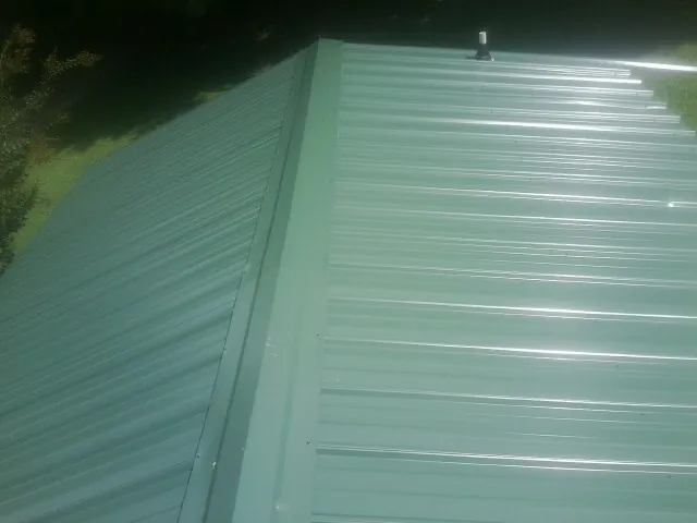 New green metal panels meeting at the ridge of a roof — Flat Roof Repair work by our crew in Kittrell