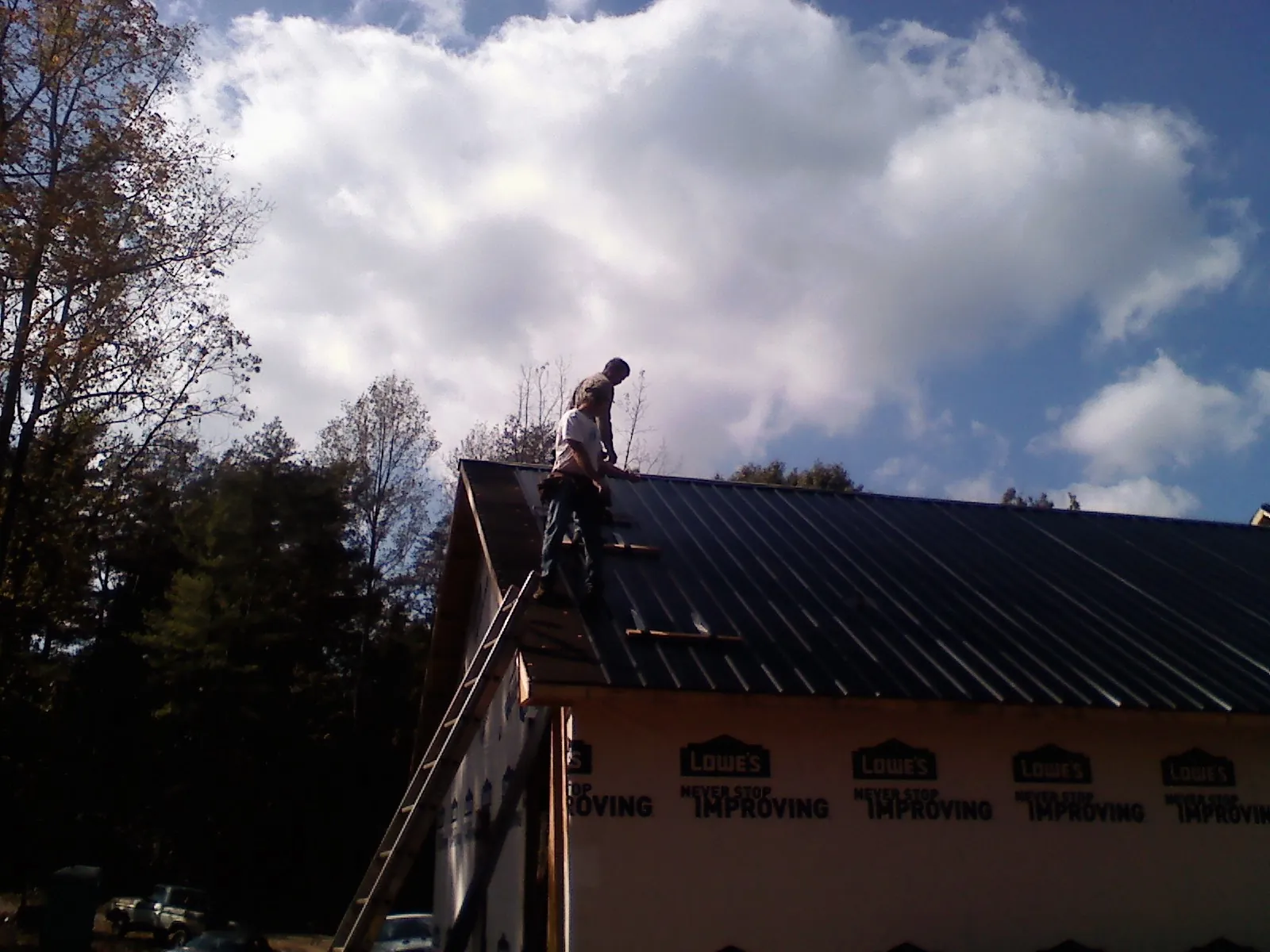 Roofer fastening dark metal panels high against a cloudy sky, from a Roof Inspection job in Kittrell