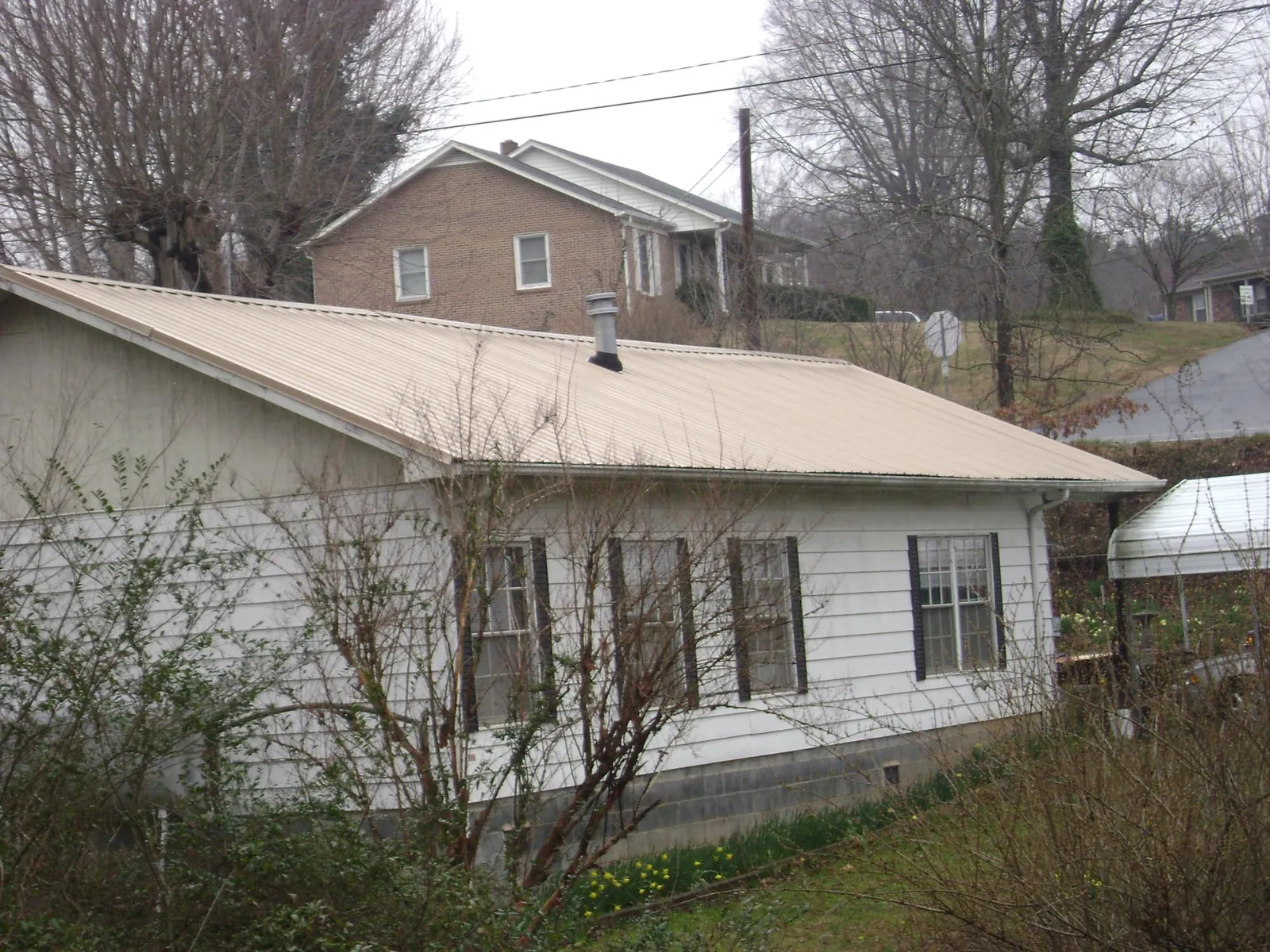 Tan metal roof on a white sided house set into a hillside — Commercial Roofing by Roofing Brothers in Kittrell