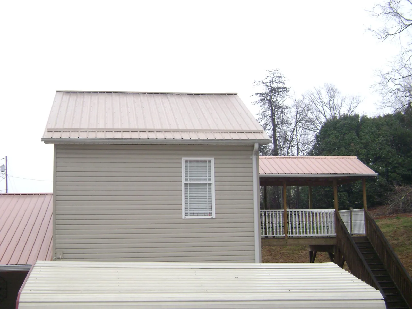 Tan metal roofs on a two story addition and attached porch, from a Roof Replacement job in Kittrell